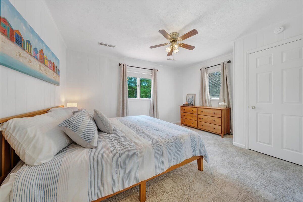 A bedroom with a bed, a dresser, a ceiling fan, and a door.