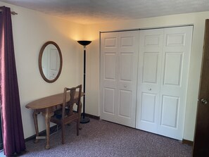 A room with a wooden desk, a chair, a floor lamp, and a closed white door.