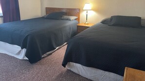 Quarto de hotel com duas camas, uma mesinha de cabeceira com abajur e quadros nas paredes.