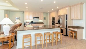 A modern kitchen with light-colored cabinets, stainless steel appliances, and a central island with bar stools.