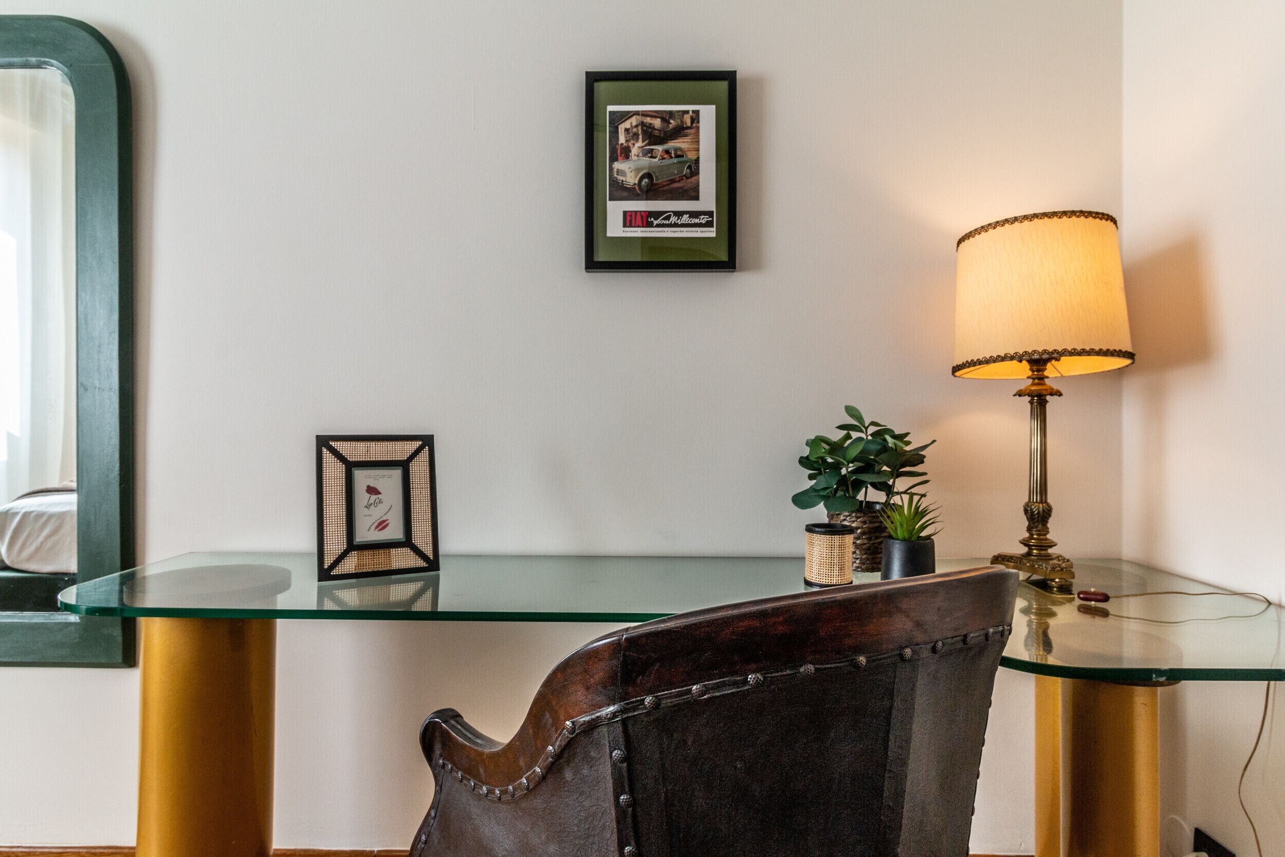 A room with a glass table, a lamp, a framed picture, and a chair.