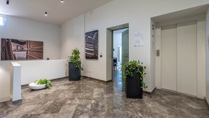 Un corridoio moderno con pavimento in marmo, fioriere nere con piante verdi e opere d'arte alle pareti.