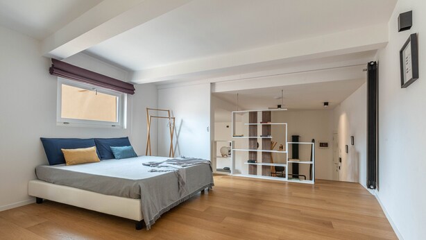 Una camera da letto moderna con un letto grande, pavimento in legno, una finestra con persiane e una libreria a muro.
