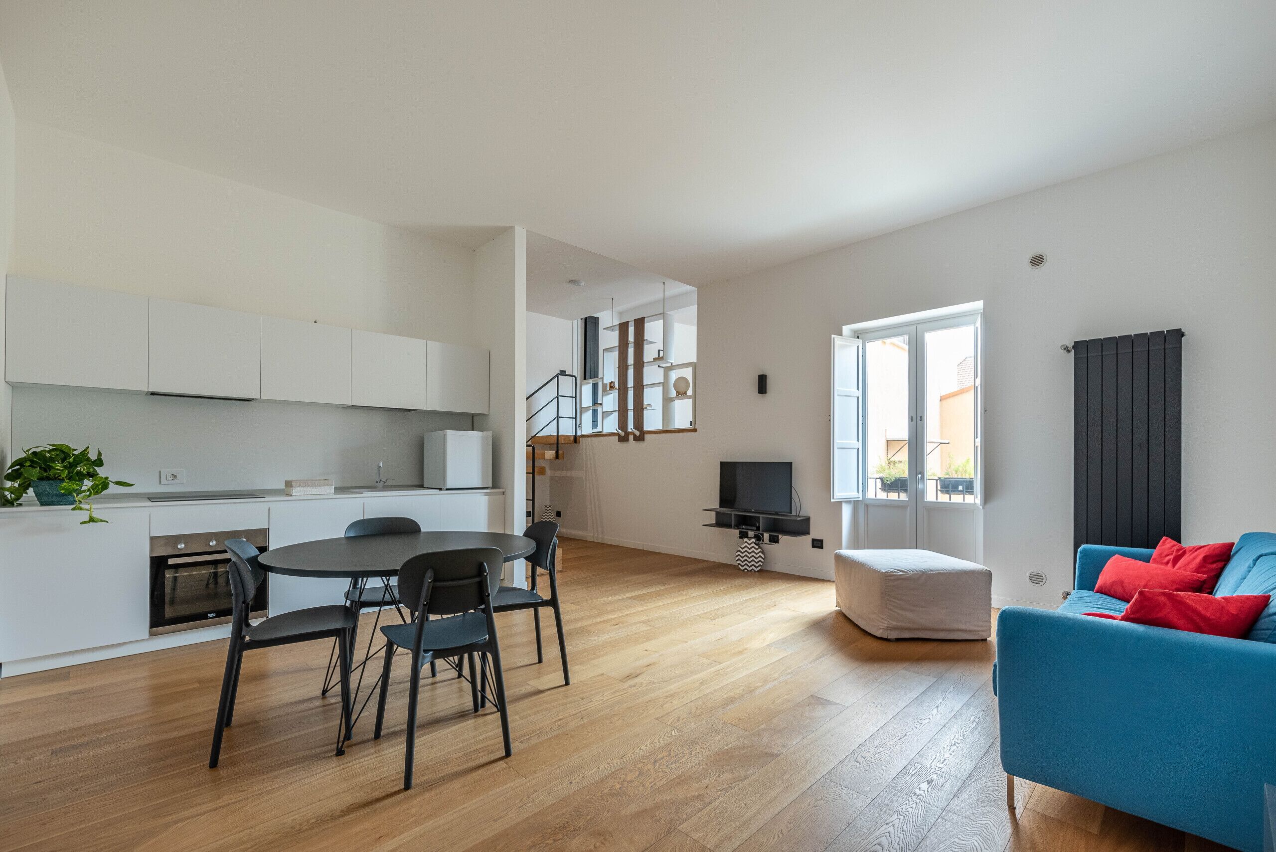 Een modern appartement met keuken, eethoek, woonkamer en een trap naar een verdieping.
