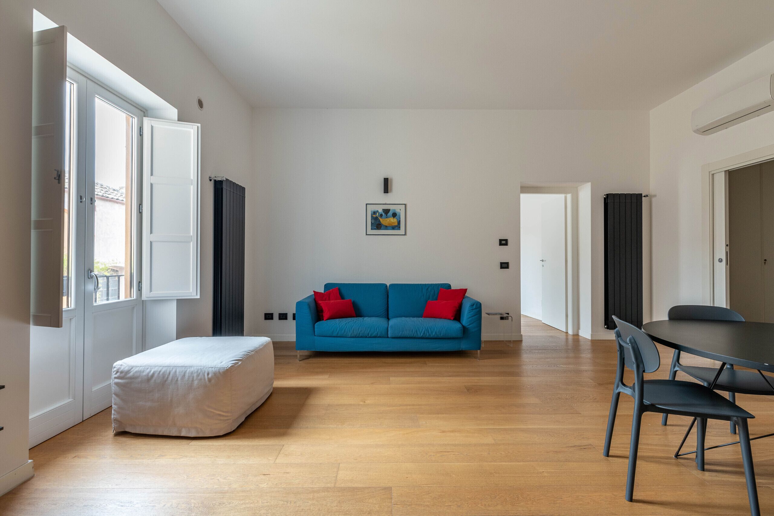 Een ruime woonkamer met een blauwe bank, een klein voetenbankje en een eettafel met stoelen.