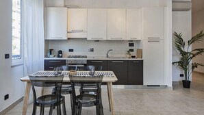 A modern kitchen with white cabinets, a gas stove, and a dining area with a table and chairs. - Shelley Apartments - Tree by Wonderful Italy (Genova)