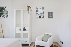 A bedroom with a white wardrobe, a white chair, and two framed pictures on the wall.