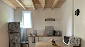 Una cocina pequeña con techo de madera, ventana, lavamanos, microondas y refrigerador.