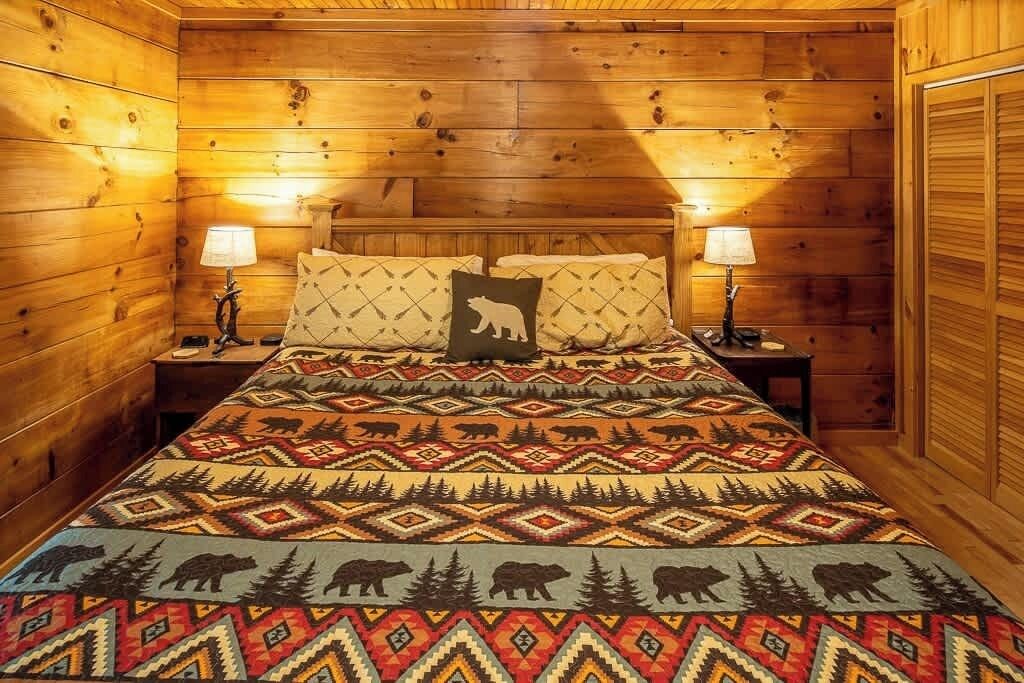 A wooden cabin room with a bed, two nightstands, and two lamps.