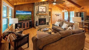 Een gezellig interieur van een chalet met een stenen openhaard, een grote flatscreen televisie, houten wanden en een comfortabele zithoek.