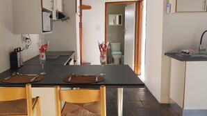 A dining area with a black table, two chairs, and a kitchen in the background. - Country Cottage in Conservation Area off Pari Park (Gqeberha)