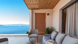 A balcony with a view of the sea, wicker furniture, and a wooden door. - DEL MARE SUITES (Stylida)