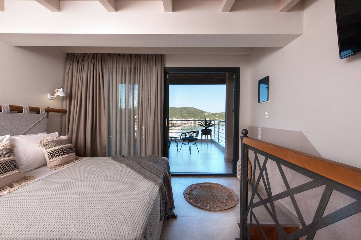 A bedroom with a bed, a view of the balcony, and a dining area outside.