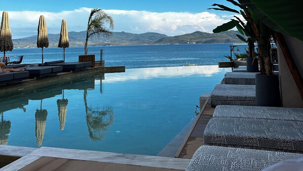 A poolside area with lounge chairs, umbrellas, and a view of the sea and mountains. - DEL MARE SUITES (Stylida)