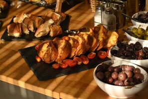 A buffet table with various food items including bread, tomatoes, olives, and grapes. - DEL MARE SUITES (Stylida)