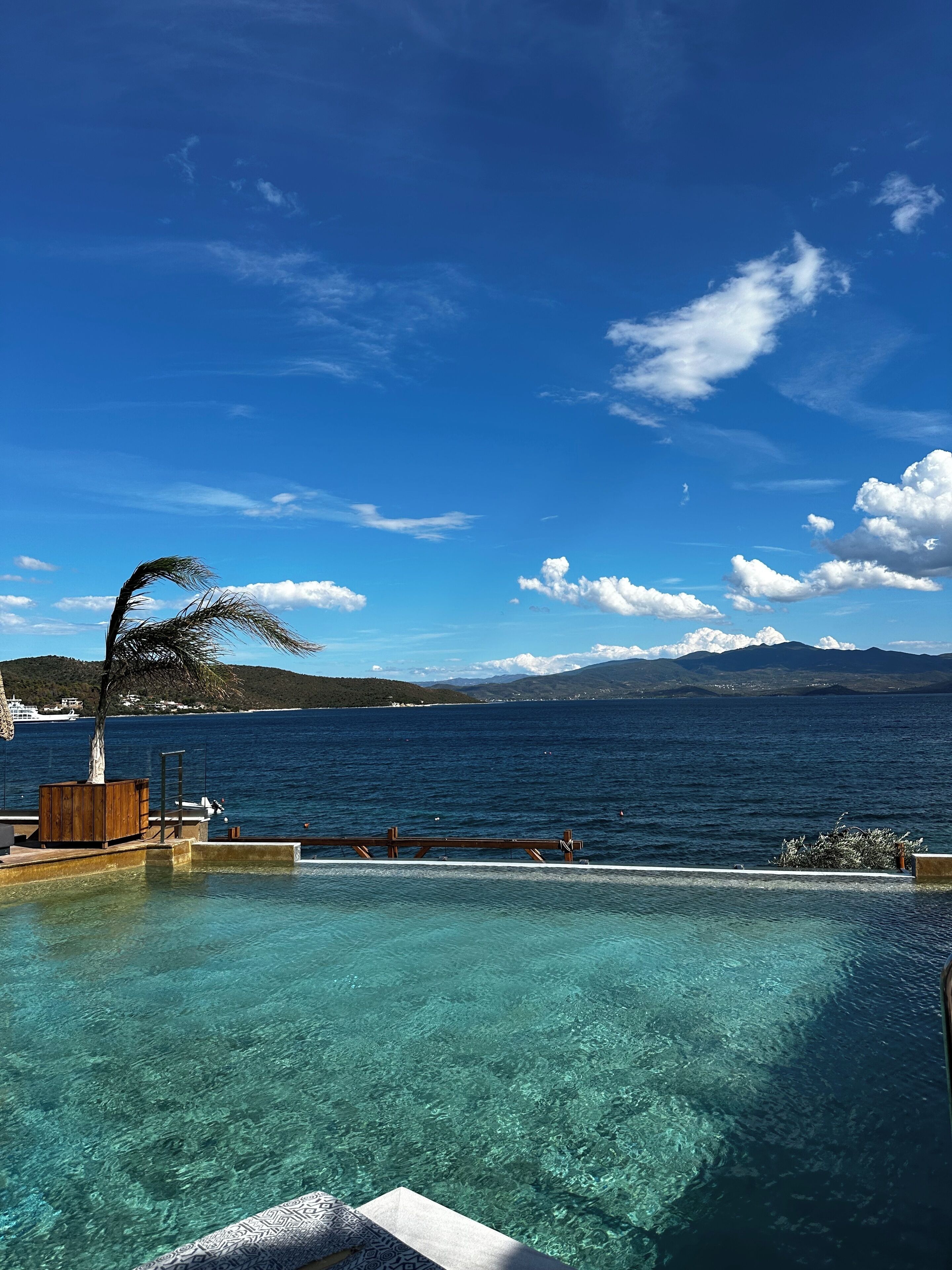 Un ciel d’un bleu limpide, une mer calme et une terrasse en bois avec une piscine.