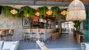 A bar area with a long counter, multiple stools, and hanging plants. - DEL MARE SUITES (Stylida)