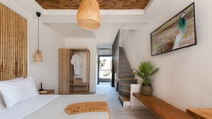 A modern bedroom with a large bed, a wooden wardrobe, a hanging light fixture, and a staircase leading to a balcony. - DEL MARE SUITES (Stylida)