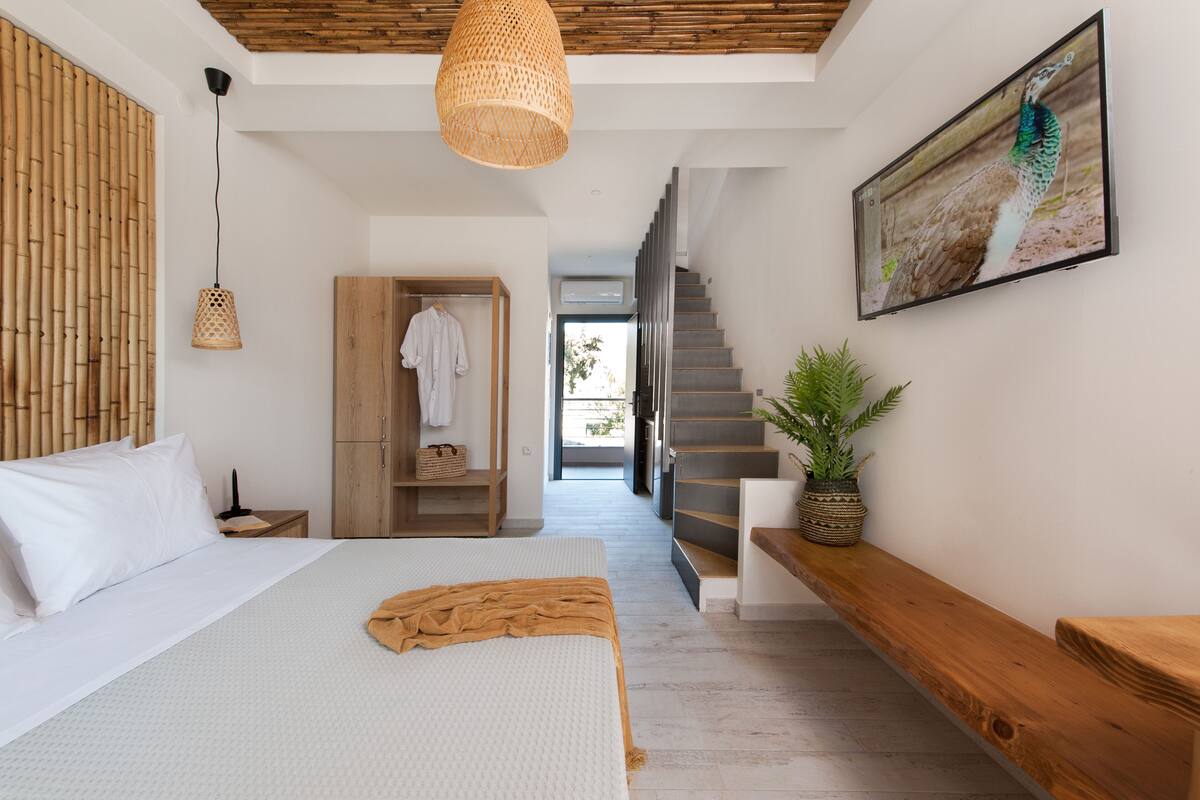 A modern bedroom with a large bed, a wooden wardrobe, a hanging light fixture, and a staircase leading to a balcony.