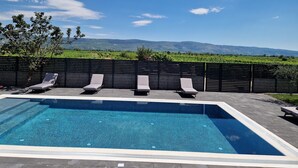 A rectangular swimming pool with a tiled edge, surrounded by a dark fence. There are three lounge chairs aligned along the fence, and a tree is visible to the left of the pool. - Luxury villa with private swimming pool (Zmijavci)