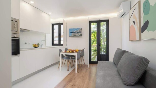 Une cuisine moderne avec des meubles blancs, une table à manger avec des chaises et un canapé gris.