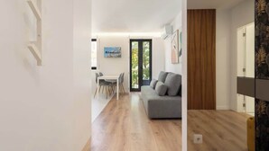 Un salon moderne avec un canapé gris, un plancher en bois et un coin repas comprenant une table et des chaises blanches.