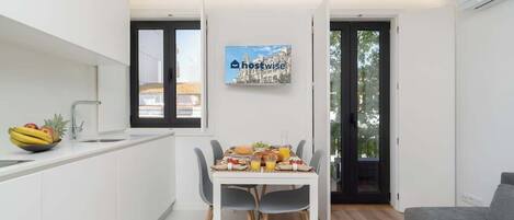 A modern kitchen with a dining table set for breakfast, a bowl of fruit, and a painting on the wall.