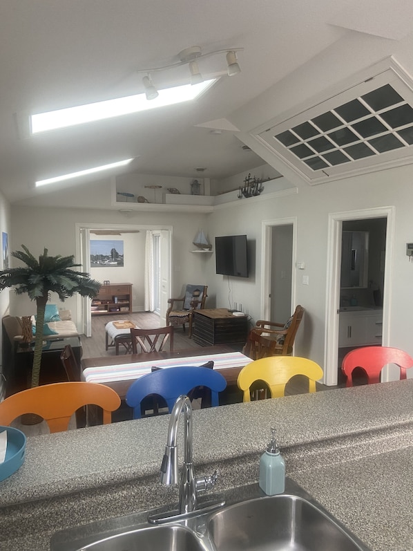 Cozinha moderna com bancada de granito, pia de aço inoxidável e área de refeições com cadeiras coloridas.