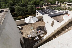 Una terraza en la azotea con mesa y sillas, un paraguas blanco y paneles solares.