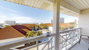 Ein Balkon mit Blick auf eine Küstenlandschaft, mit Gebäuden mit roten Ziegeldächern und Palmen.