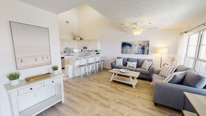 Ein modernes Wohnzimmer mit grauem Sofa, einem Couchtisch und einer Küche im Hintergrund.