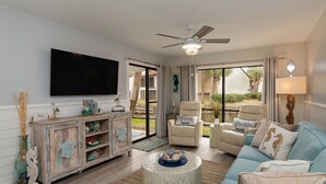 Una sala de estar con televisor, ventilador de techo, sofá, sillón y una mesa de centro.