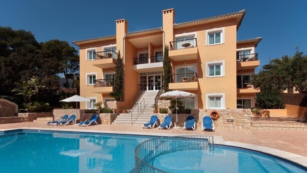 Et hotel med flere etager, en swimmingpool, liggestole og en trappe til indgangen.