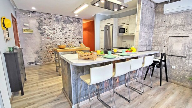 Una cucina moderna con isola centrale, sgabelli da bar e una parete decorativa in pietra.