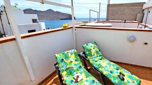 Un balcone con due lettini, un tavolino rotondo e vista sul mare e sulle montagne.