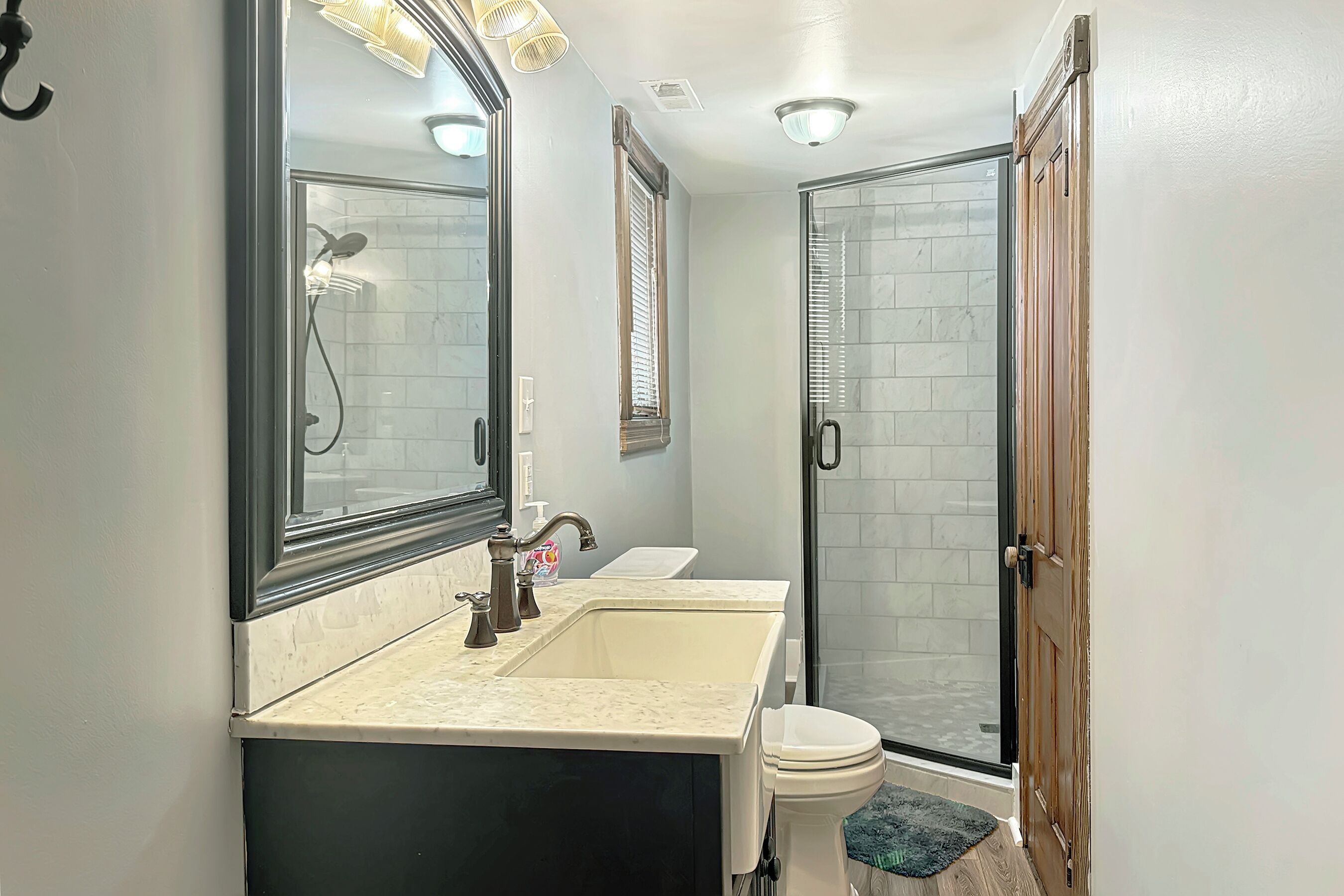 A bathroom with a double sink, a toilet, a glass shower enclosure, and a wooden door.