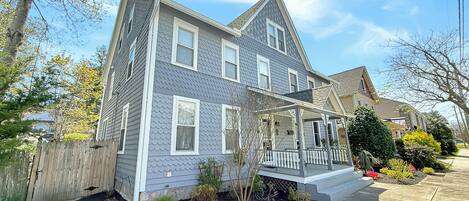 A two-story house with a front porch, a wooden fence, and a landscaped garden with various plants and flowers.