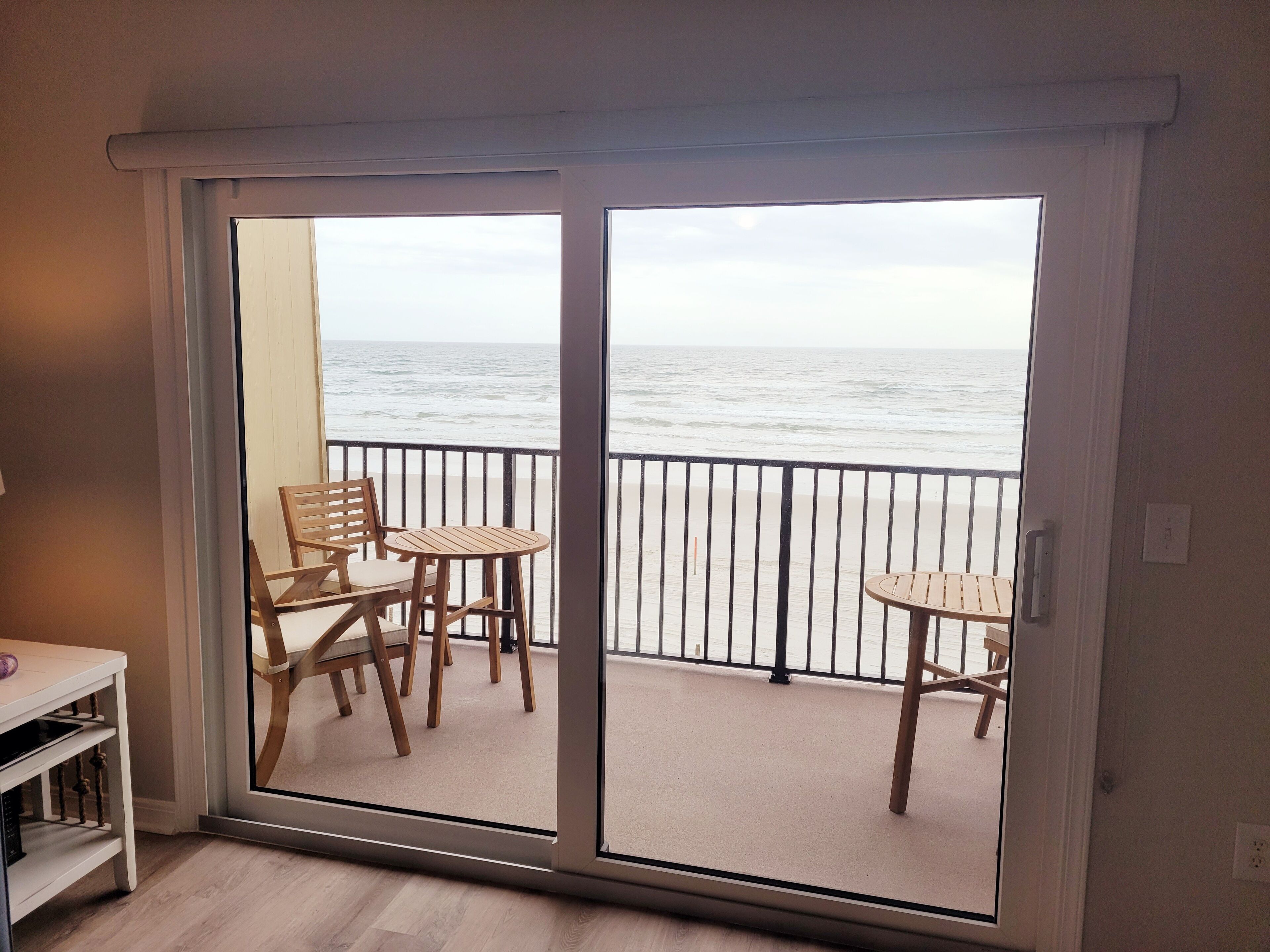 A balcony with a view of the ocean, furnished with wooden chairs and a small table.