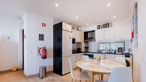 Une cuisine moderne avec des meubles blancs, une table à manger pour deux personnes et un extincteur fixé au mur.