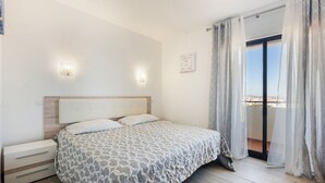 Une chambre à coucher avec un lit, des tables de chevet, une fenêtre avec des rideaux et une vue sur l’extérieur.