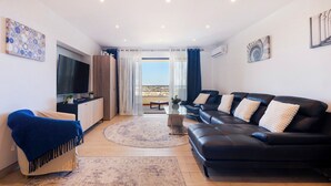 Un salon moderne avec un canapé, un téléviseur, une table basse et une vue sur l’extérieur.