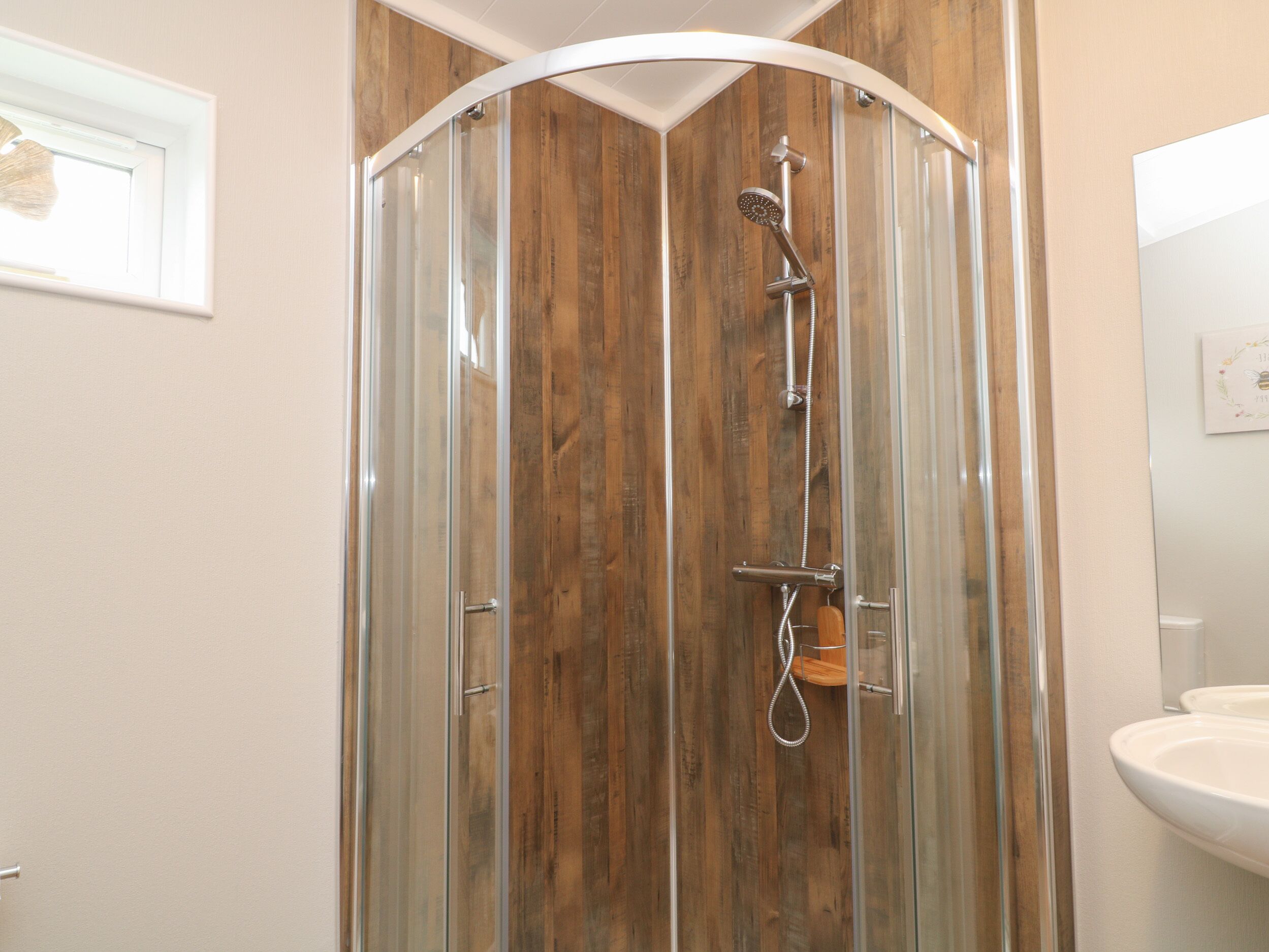 A glass-enclosed shower stall with a wooden panel wall, a handheld showerhead, and a handheld shower attachment.