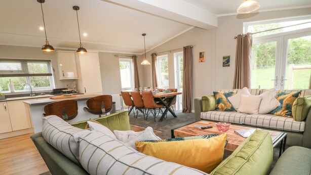 A modern living room with a sofa, a dining area, and a kitchen. - Lily (Lifton)