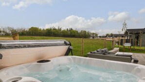 A hot tub with a control panel, surrounded by outdoor furniture and a grassy area with a fence and trees in the background. - Lily (Lifton)