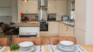 A modern kitchen with a central island, stainless steel appliances, and a dining area with a table set for two. - Lily (Lifton)