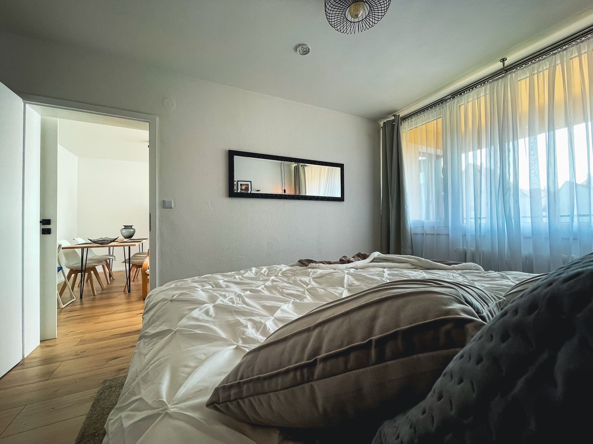 Ein Schlafzimmer mit einem großen Bett, einem Nachttisch, einem Spiegel und einem Fenster mit Vorhängen.