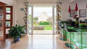 A modern kitchen with a green countertop, a bar area with stools, and a view of a garden through an open door.