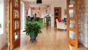 A spacious living area with wooden flooring, a large potted plant, and a kitchen in the background.