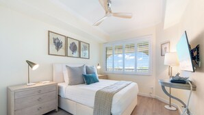 A bedroom with a bed, bedside tables, a ceiling fan, and artwork on the wall. - Beachcomber 24 by Grand Cayman Villas (7 Mile Beach)