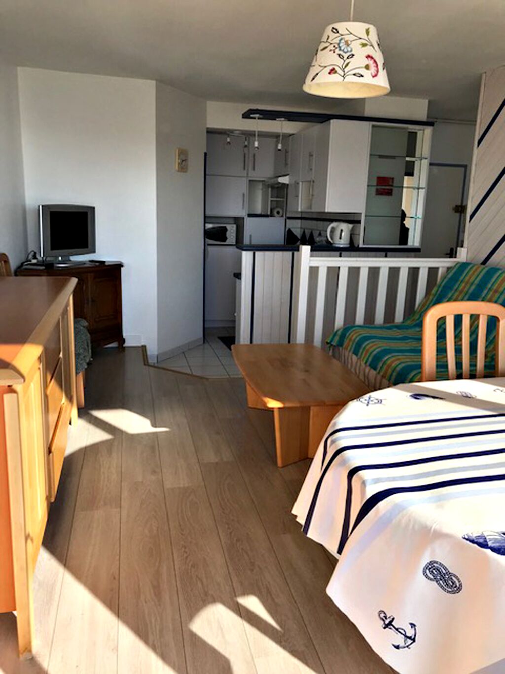 Un espacio habitable compacto con kitchenette, comedor y cama con ropa de cama de temática náutica.